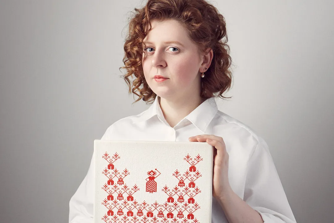 Rufina Bazlova présentant une broderie de la série “The History of Belarusian Vyzhyvanka”, motifs rouge et blanc, mémoire de la répression